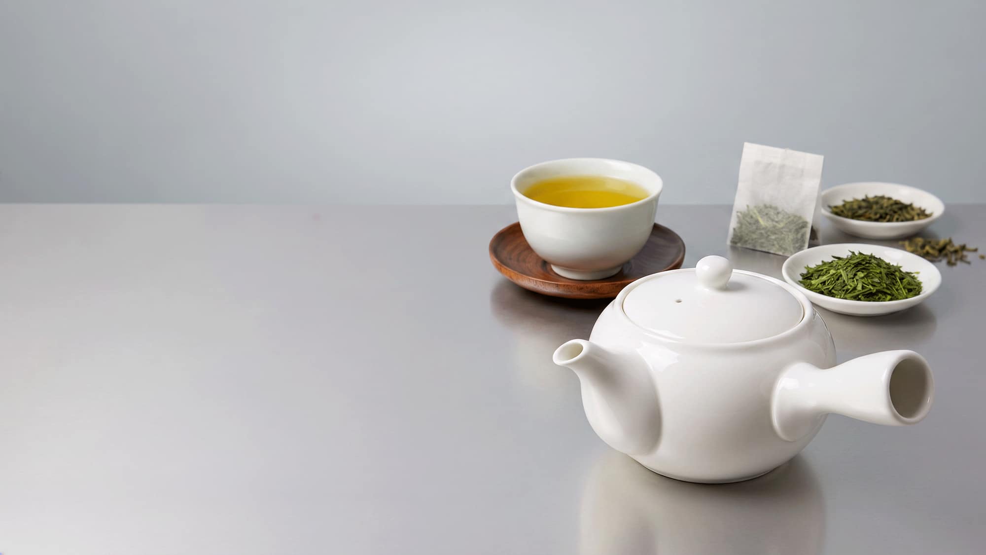 白い急須と湯呑に注がれた煎茶、木の茶托、小皿に盛られた茶葉