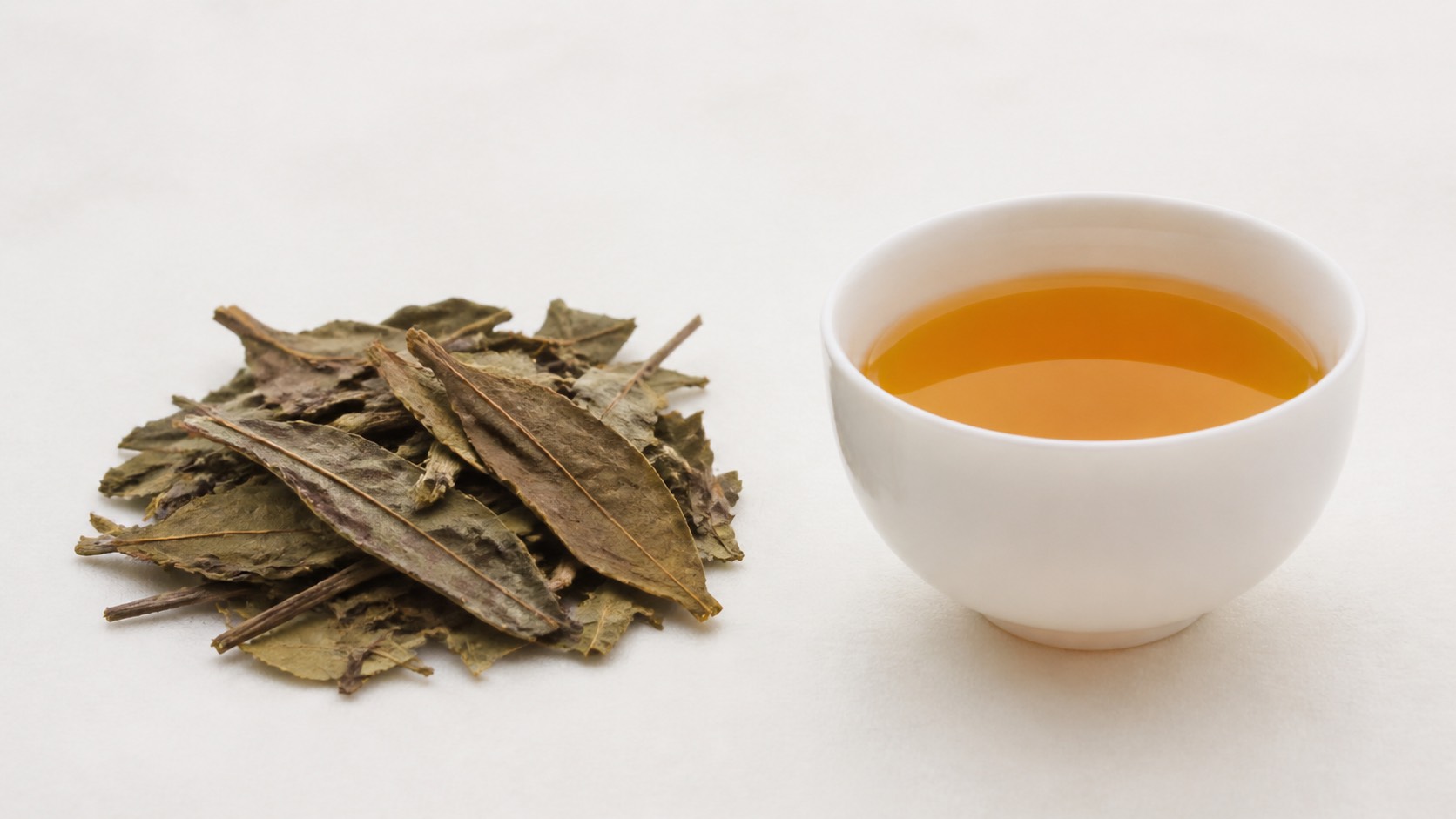大きく平たい番茶の葉と茎、白い湯呑に注がれた透明な淡い金褐色の水色
