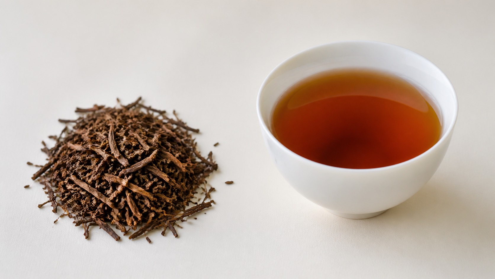 赤褐色に焙じられたほうじ茶の茎と葉、白い湯呑に注がれた透明な赤褐色の水色
