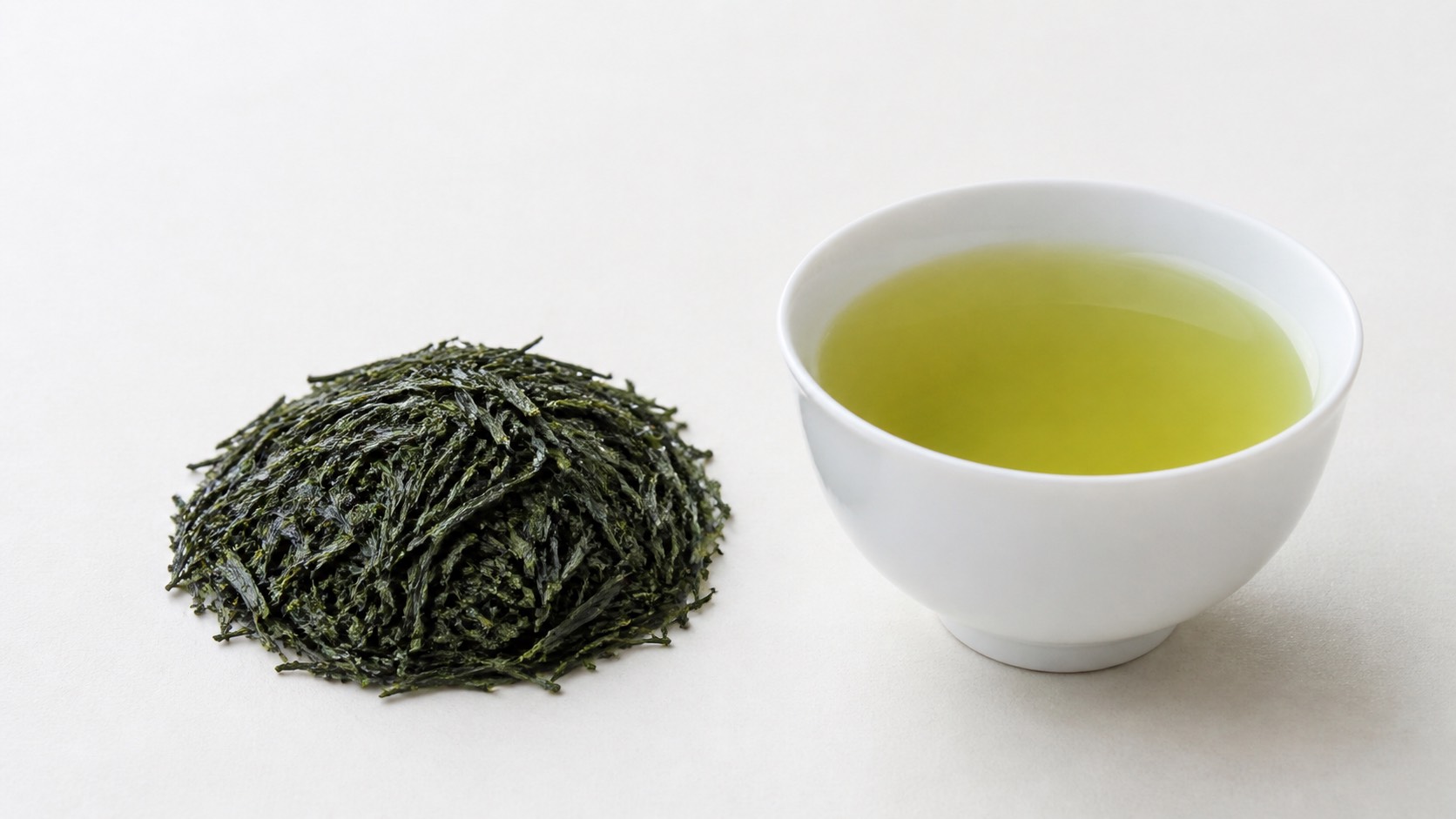 濃い緑のかぶせ茶の茶葉と、白い湯呑に注がれたやや濃い黄緑の水色