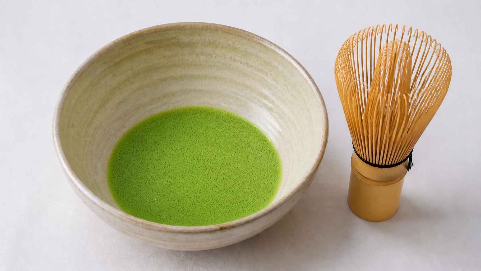 浅く広い茶碗に点てられた薄茶。表面が細かい泡で覆われ、脇に穂の多い茶筅が立てられている
