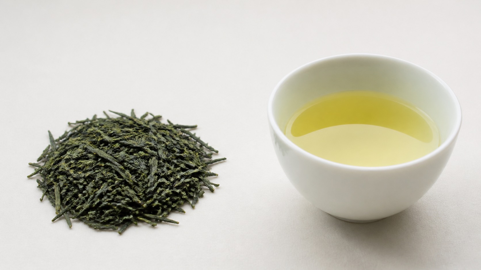 針状に伸びた濃い緑の煎茶の茶葉と、白い湯呑に注がれた透明な淡い黄緑の水色